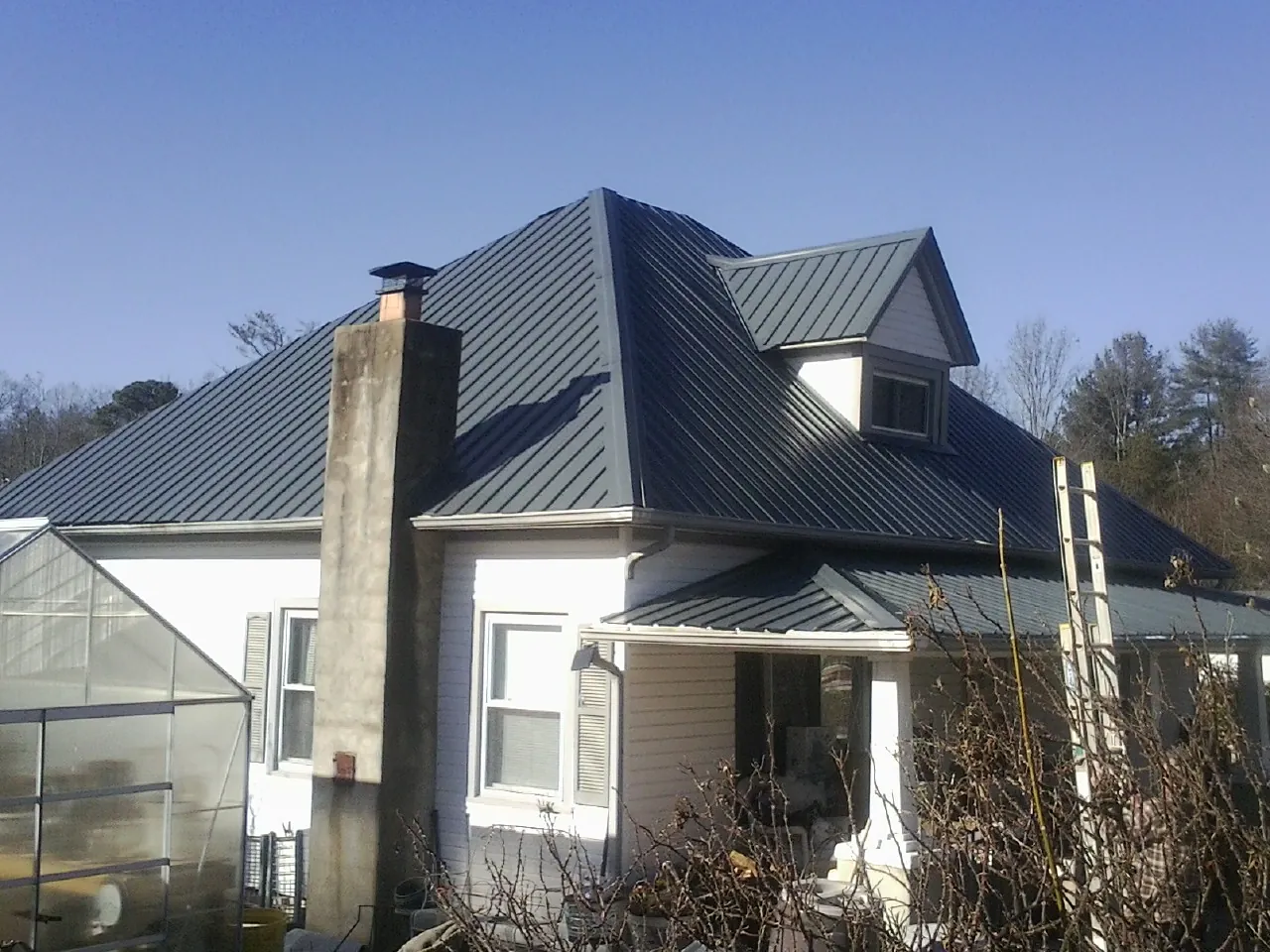Dark blue standing seam metal roof on a white farmhouse with dormer — Slate & Tile Roof Repair by Roofing Brothers in Mary Esther