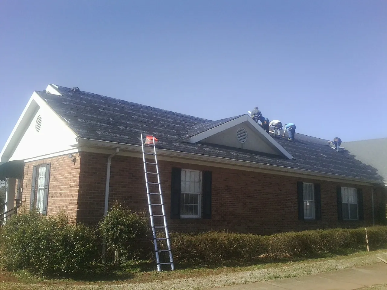 Crew tearing shingles off a brick ranch roof with a ladder set — Metal Roof Repair work by our crew in Mary Esther