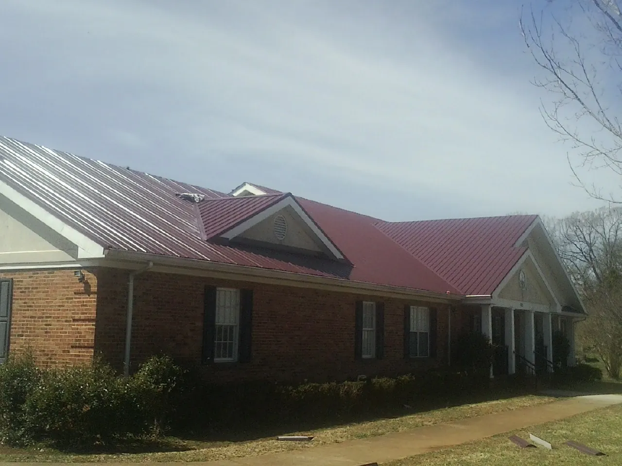 Red metal roof with gabled entries on a long brick building, from a Hail Damage Roof Repair job in Mary Esther
