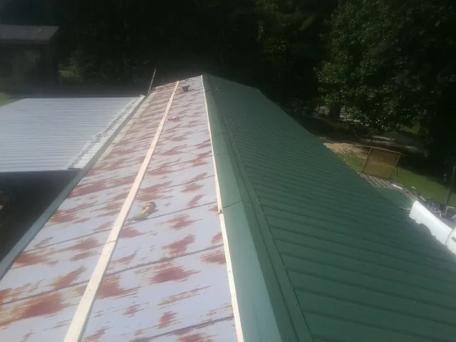 Old rusted panels beside newly installed green metal roofing — Wind Damage Roof Repair by Roofing Brothers in Mary Esther