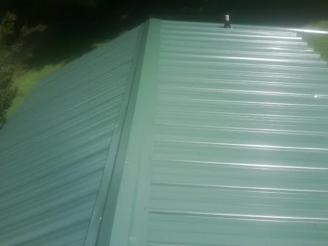 New green metal panels meeting at the ridge of a roof — Flat Roof Repair work by our crew in Mary Esther
