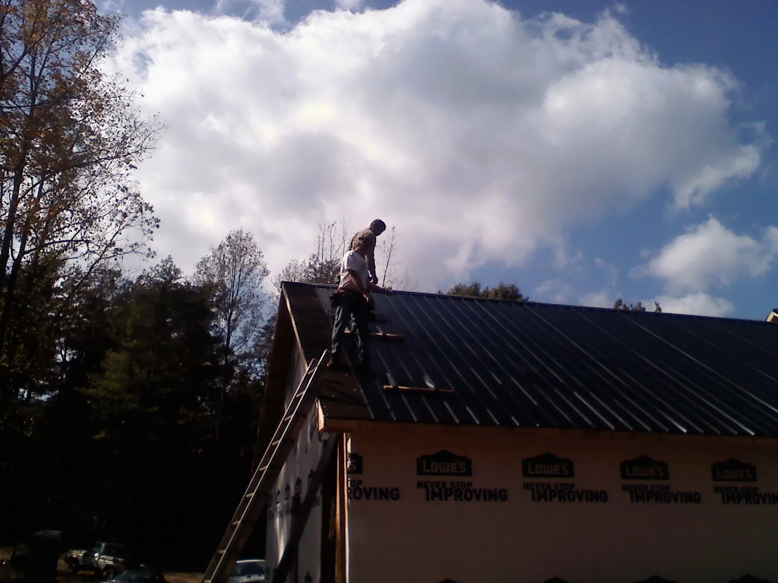 Roofer fastening dark metal panels high against a cloudy sky, from a Roof Inspection job in Mary Esther