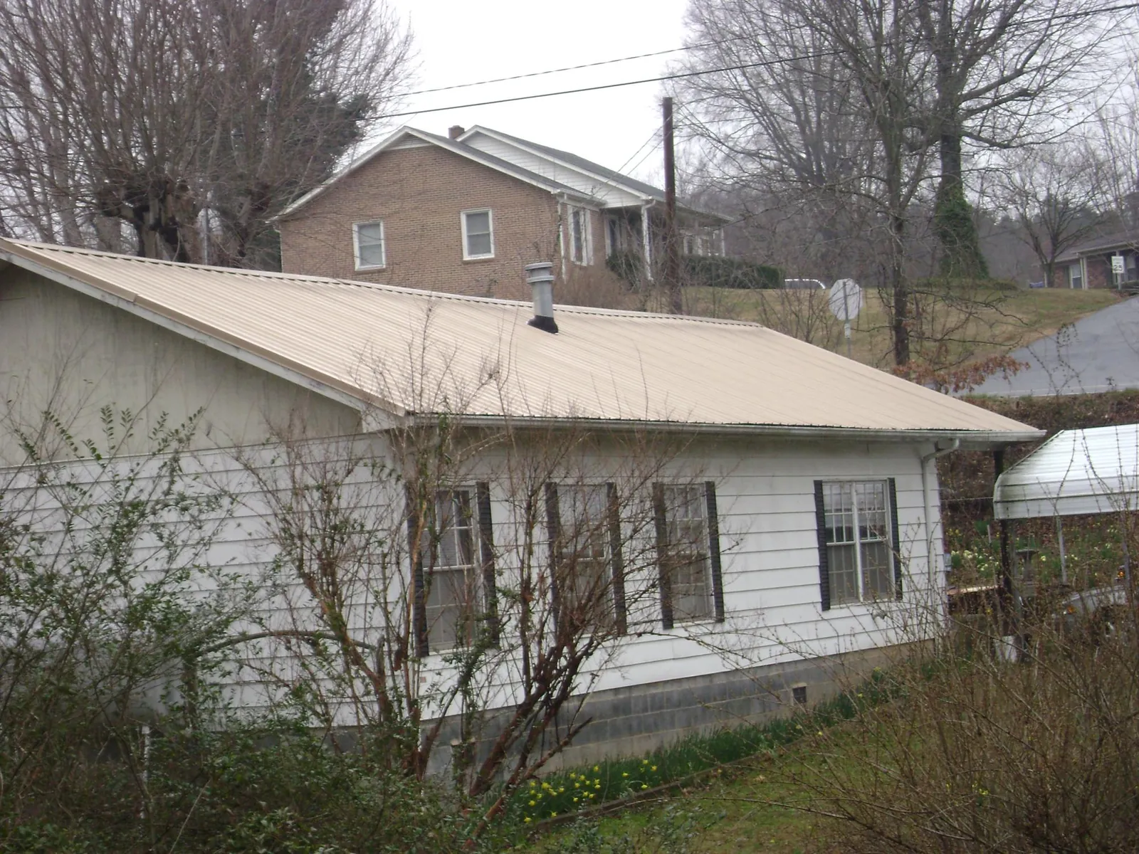 Tan metal roof on a white sided house set into a hillside — Commercial Roofing by Roofing Brothers in Mary Esther