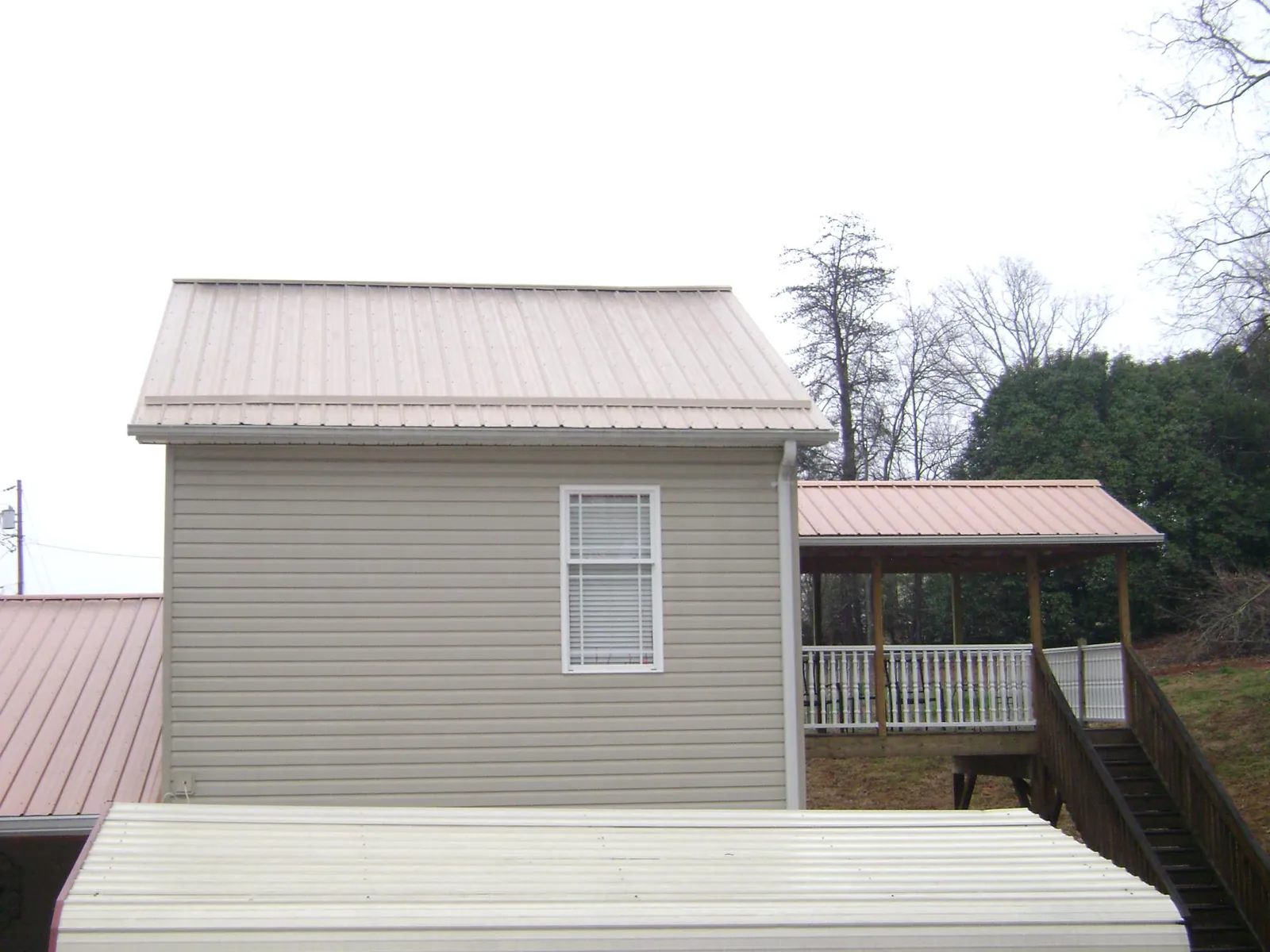 Tan metal roofs on a two story addition and attached porch, from a Roof Replacement job in Mary Esther